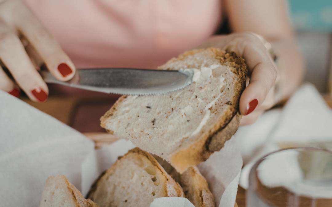 Woman's hands holding piece of bread and knife spreading butter